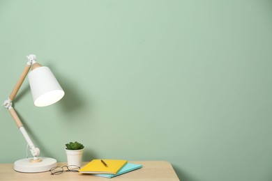 Photo of Stylish workplace with lamp, stationery and plant on wooden desk near light green wall. Space for text