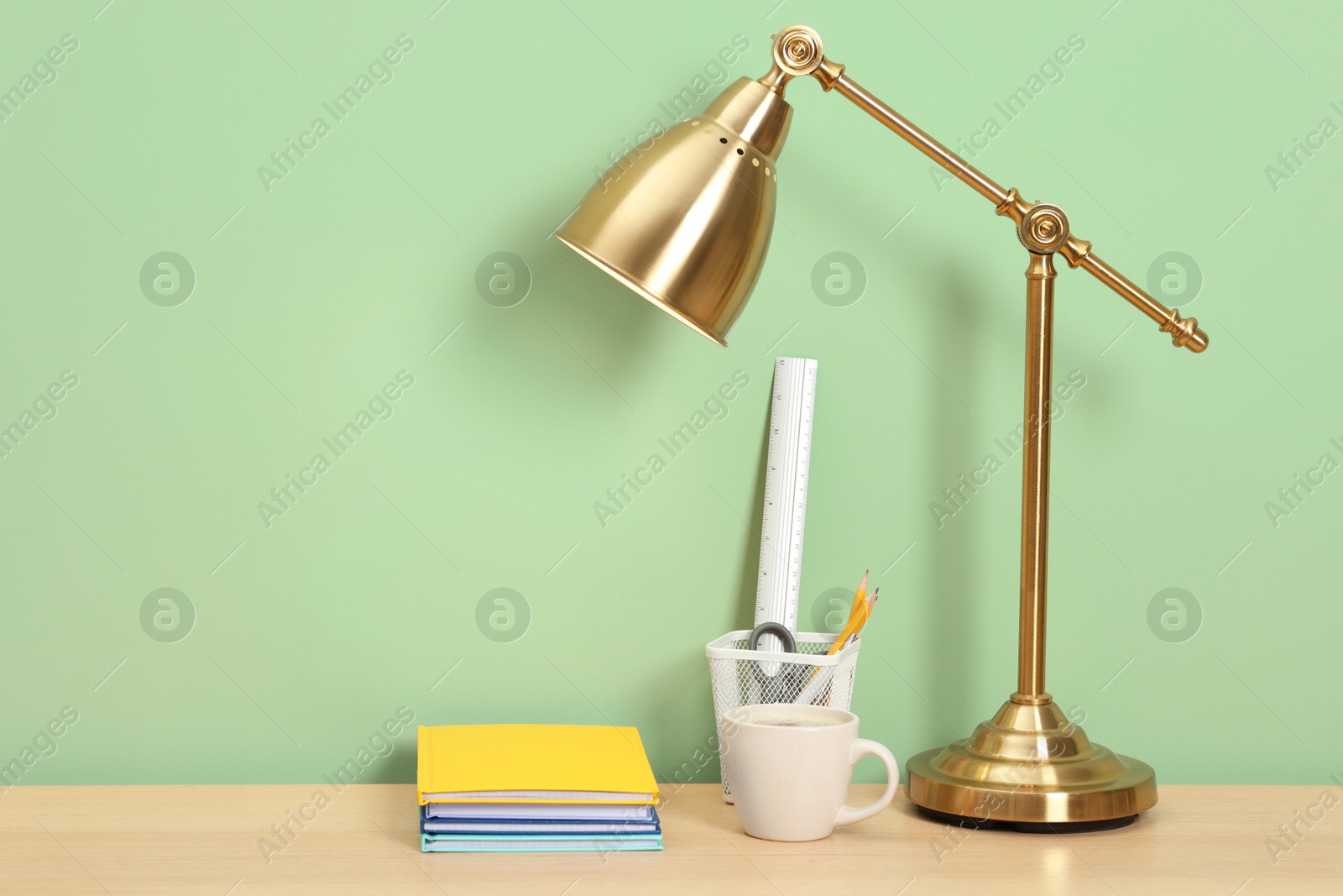 Stylish workplace with lamp, stationery and coffee on wooden desk near light green wall. Space for text Photo of Stylish workplace with lamp, stationery and coffee on wooden desk near light green wall. Space for text