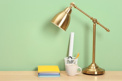 Photo of Stylish workplace with lamp, stationery and coffee on wooden desk near light green wall. Space for text