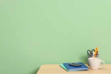 Photo of Stylish workplace with stationery and coffee on wooden desk near light green wall. Space for text