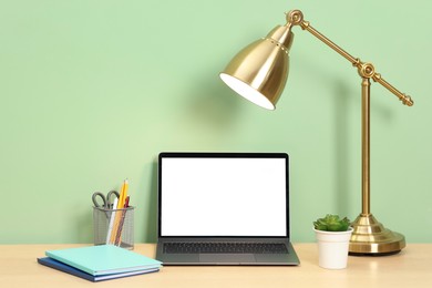 Photo of Stylish workplace with modern laptop on wooden desk near light green wall