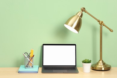 Photo of Stylish workplace with modern laptop on wooden desk near light green wall