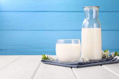 Photo of Fresh milk and blossoms on white wooden table against light blue background, closeup. Space for text