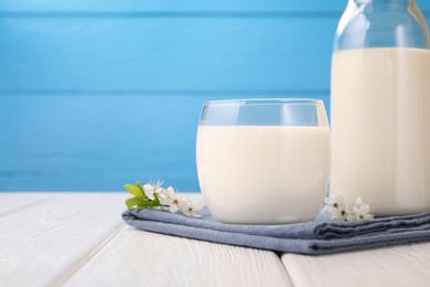 Photo of Fresh milk and blossoms on white wooden table against light blue background, closeup. Space for text