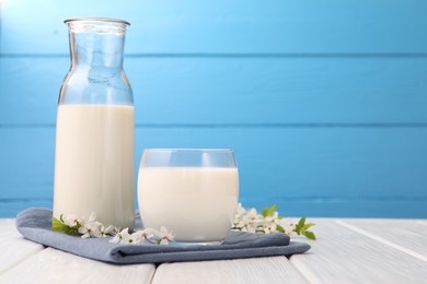Photo of Fresh milk and blossoms on white wooden table against light blue background, closeup. Space for text