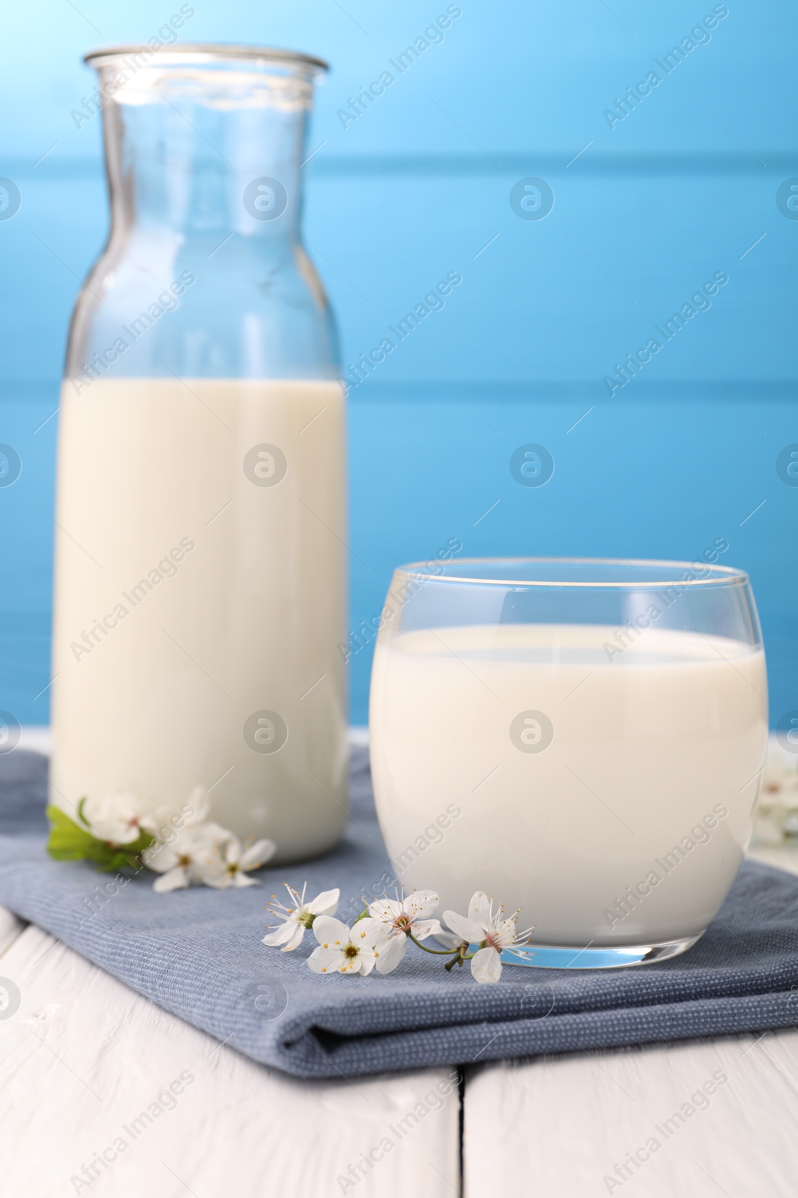 Fresh milk and blossoms on white wooden table against light blue background, closeup Photo of Fresh milk and blossoms on white wooden table against light blue background, closeup