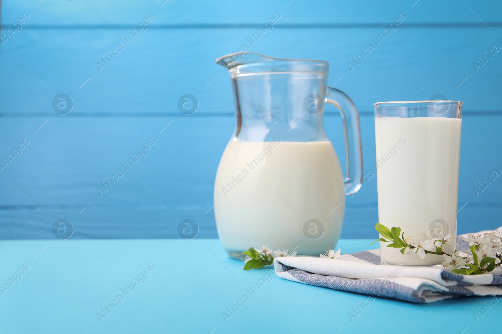Fresh milk and blossoms on light blue table, closeup. Space for text Photo of Fresh milk and blossoms on light blue table, closeup. Space for text