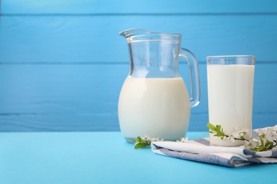 Photo of Fresh milk and blossoms on light blue table, closeup. Space for text