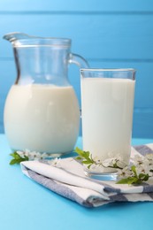 Photo of Fresh milk and blossoms on light blue table, closeup