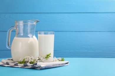 Photo of Fresh milk and blossoms on light blue table. Space for text