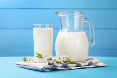 Photo of Fresh milk and blossoms on light blue table, closeup