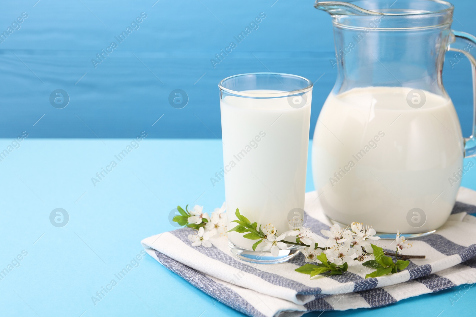 Fresh milk and blossoms on light blue table, closeup. Space for text Photo of Fresh milk and blossoms on light blue table, closeup. Space for text