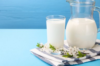 Photo of Fresh milk and blossoms on light blue table, closeup. Space for text