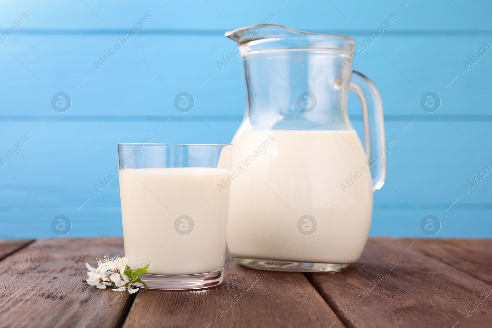 Fresh milk and blossoms on wooden table against light blue background, closeup Photo of Fresh milk and blossoms on wooden table against light blue background, closeup