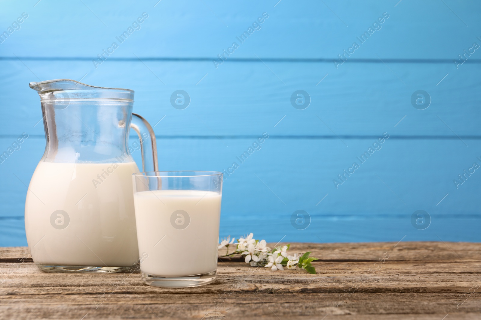 Fresh milk and blossoms on wooden table against light blue background. Space for text Photo of Fresh milk and blossoms on wooden table against light blue background. Space for text