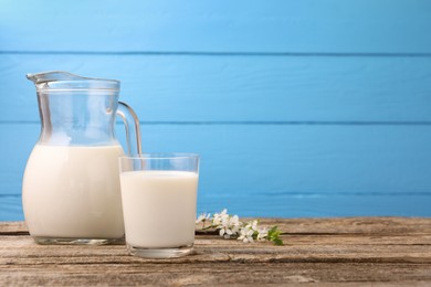 Photo of Fresh milk and blossoms on wooden table against light blue background. Space for text