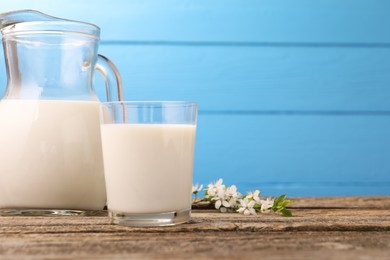 Photo of Fresh milk and blossoms on wooden table against light blue background, closeup. Space for text
