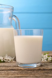 Photo of Fresh milk and blossoms on wooden table against light blue background, closeup
