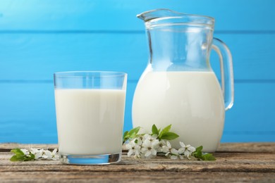 Photo of Fresh milk and blossoms on wooden table against light blue background, closeup