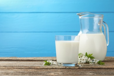 Photo of Fresh milk and blossoms on wooden table against light blue background. Space for text
