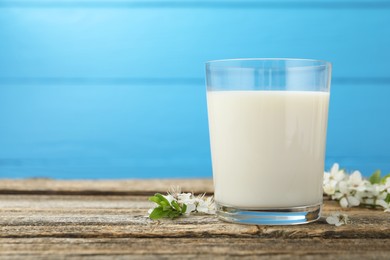 Photo of Fresh milk in glass and blossoms on wooden table against light blue background, closeup. Space for text