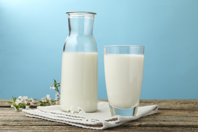 Photo of Fresh milk and blossoms on wooden table against light blue background, closeup