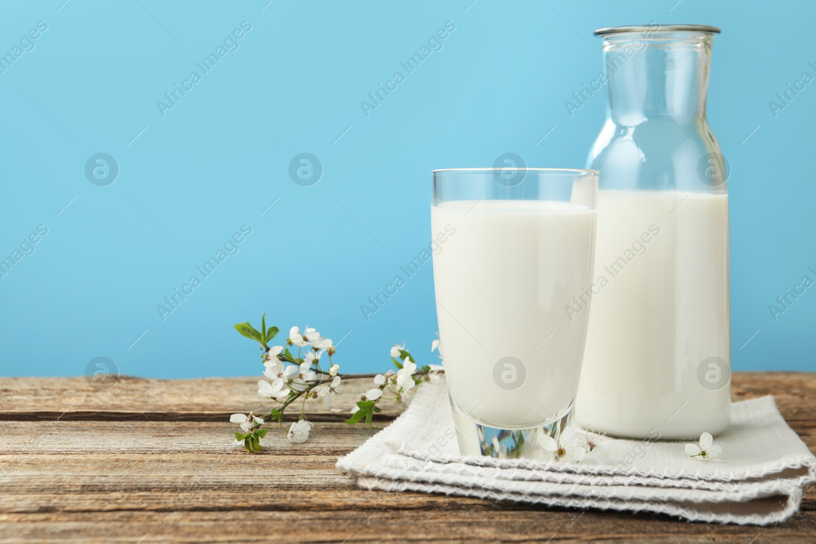 Fresh milk and blossoms on wooden table against light blue background, closeup. Space for text Photo of Fresh milk and blossoms on wooden table against light blue background, closeup. Space for text