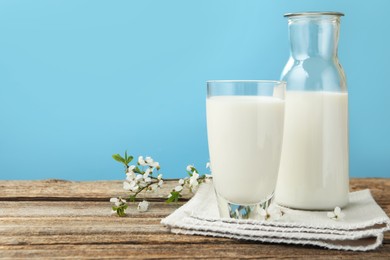 Photo of Fresh milk and blossoms on wooden table against light blue background, closeup. Space for text