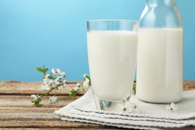 Photo of Fresh milk and blossoms on wooden table against light blue background, closeup