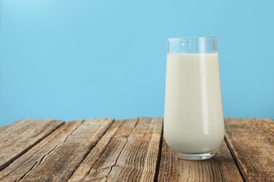Photo of Fresh milk in glass on wooden table against light blue background, closeup. Space for text