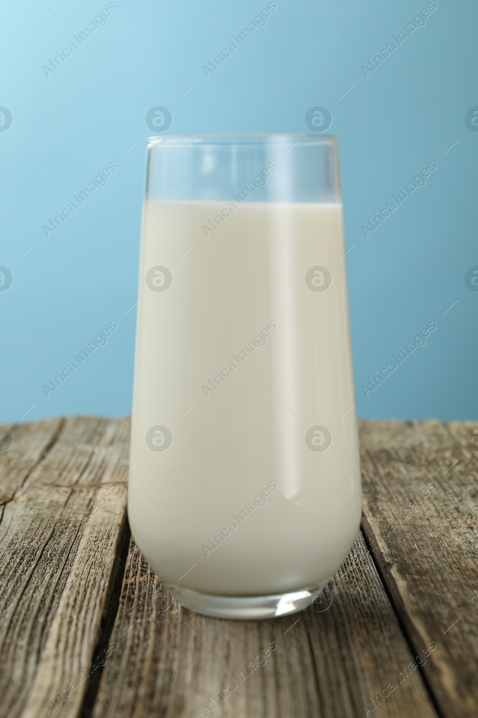 Fresh milk in glass on wooden table against light blue background, closeup Photo of Fresh milk in glass on wooden table against light blue background, closeup