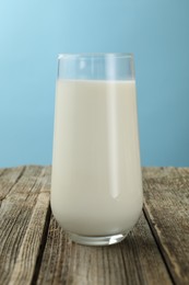 Photo of Fresh milk in glass on wooden table against light blue background, closeup