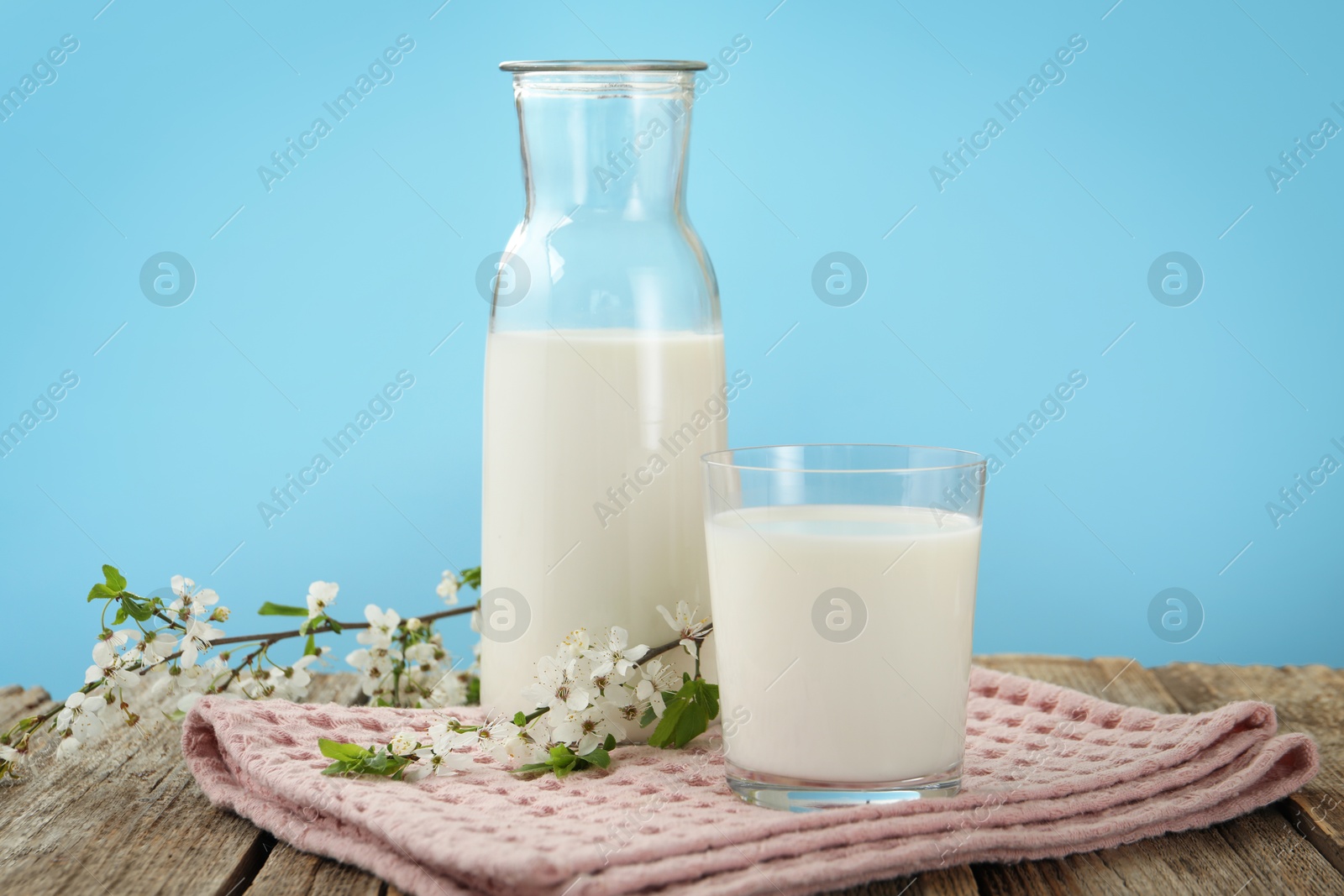 Fresh milk and blossoms on wooden table against light blue background, closeup Photo of Fresh milk and blossoms on wooden table against light blue background, closeup