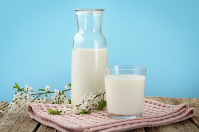 Photo of Fresh milk and blossoms on wooden table against light blue background, closeup