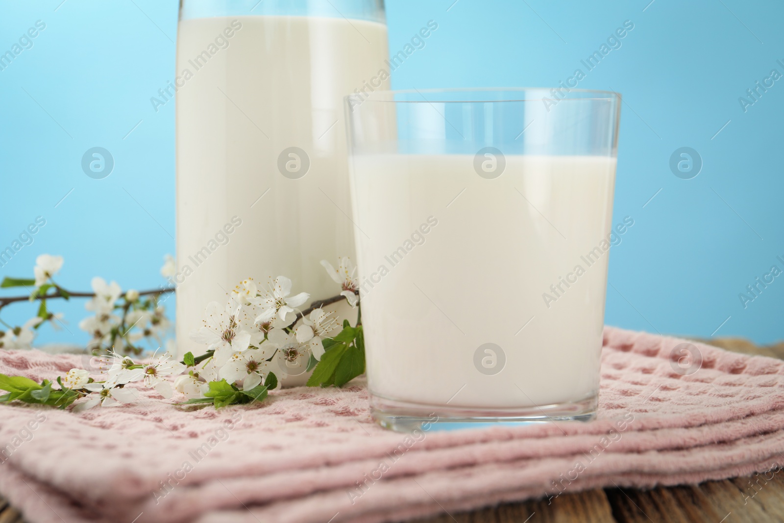 Fresh milk and blossoms on wooden table against light blue background, closeup Photo of Fresh milk and blossoms on wooden table against light blue background, closeup