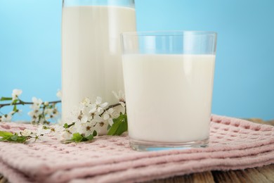 Photo of Fresh milk and blossoms on wooden table against light blue background, closeup