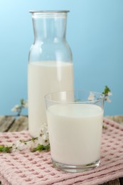 Photo of Fresh milk and blossoms on wooden table against light blue background, closeup