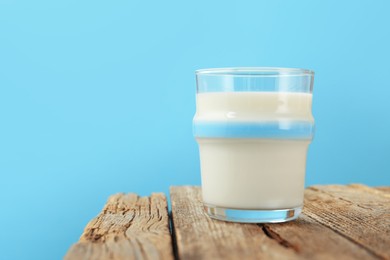 Photo of Fresh milk in glass on wooden table against light blue background, closeup. Space for text