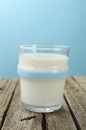 Photo of Fresh milk in glass on wooden table against light blue background, closeup