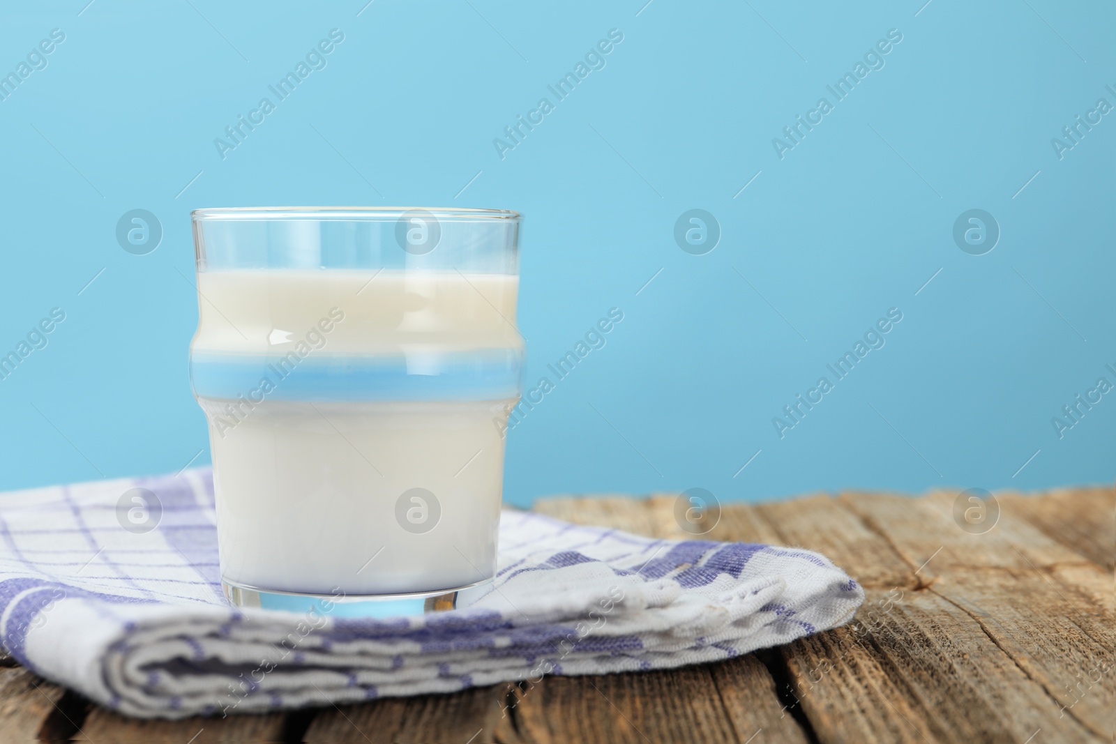 Fresh milk in glass on wooden table against light blue background, closeup. Space for text Photo of Fresh milk in glass on wooden table against light blue background, closeup. Space for text