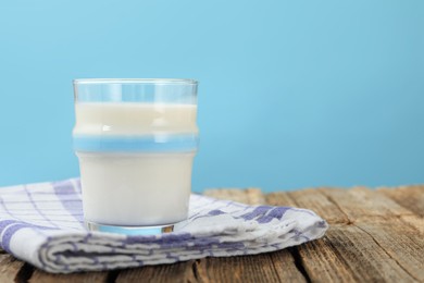 Photo of Fresh milk in glass on wooden table against light blue background, closeup. Space for text