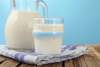 Photo of Fresh milk on wooden table against light blue background, closeup