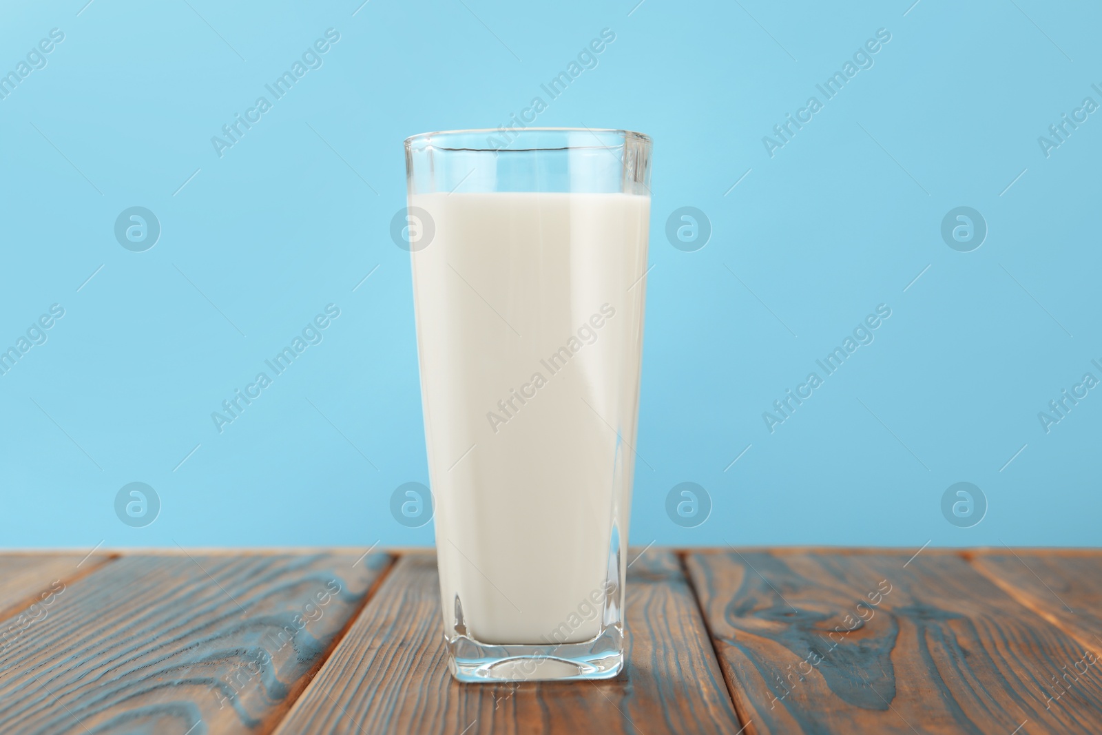 Fresh milk in glass on wooden table against light blue background, closeup Photo of Fresh milk in glass on wooden table against light blue background, closeup