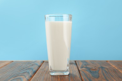 Photo of Fresh milk in glass on wooden table against light blue background, closeup