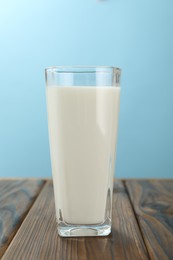 Photo of Fresh milk in glass on wooden table against light blue background, closeup