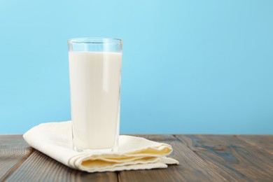 Photo of Fresh milk in glass on wooden table against light blue background, closeup. Space for text