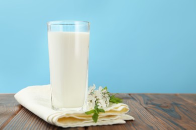 Photo of Fresh milk in glass and blossoms on wooden table against light blue background, closeup. Space for text