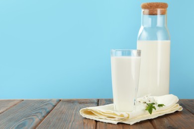 Photo of Fresh milk and blossoms on wooden table against light blue background, closeup. Space for text
