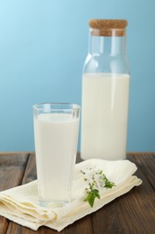 Photo of Fresh milk and blossoms on wooden table against light blue background