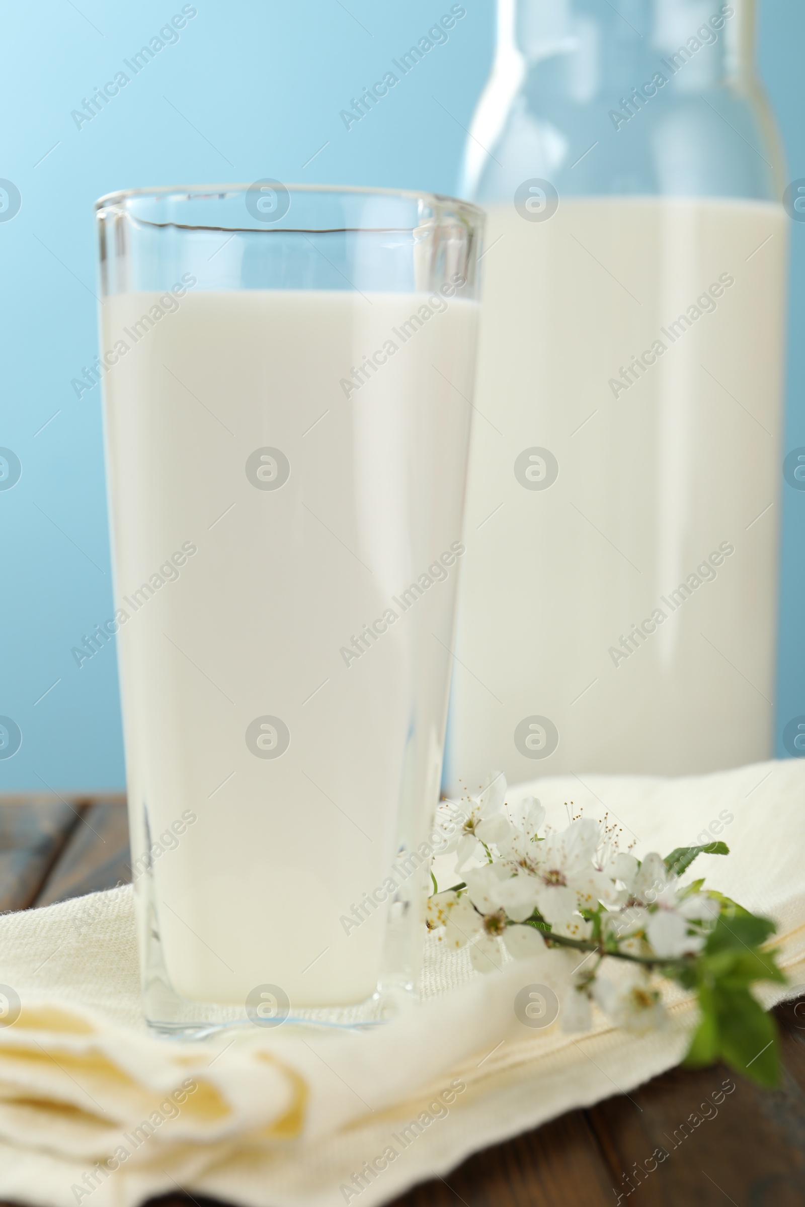 Fresh milk and blossoms on wooden table against light blue background, closeup Photo of Fresh milk and blossoms on wooden table against light blue background, closeup